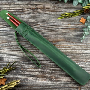 Op de afbeelding: Een groene leren drumstick-hoes met een band en het woord "MARK" erop gegraveerd.