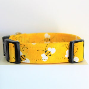 May include: A yellow dog collar with a black buckle and a pattern of bees on a white background.