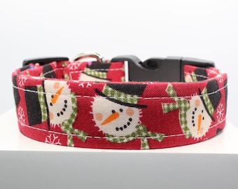 May include: Red dog collar with a snowman pattern. The collar has a black buckle and is made of fabric.