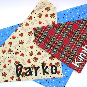 May include: Dog bandanas in various patterns. One is tan with paw prints, hearts, and bones, with the name "Darko". Another is red plaid with the name "Kimbo". A third is blue with white triangles.