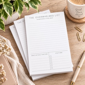 May include: A white notepad with black text titled The Overwhelmed List, Everything In My Head. The page features horizontal lines for notes, a section labeled What Actually Matters, and a section labeled Start Here with six empty checkboxes.