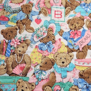 Pode incluir: Um tecido acolchoado com um padrão repetido de ursinhos de pelúcia castanhos vestidos com várias roupas. Os ursos são adornados com chapéus, laços e acessórios em cores pastel como rosa, azul e amarelo. Alguns ursos seguram corações e usam óculos.