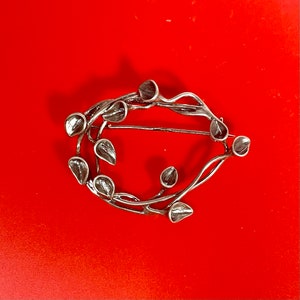 May include: A silver brooch in the shape of a stylised floral design. The brooch is made of metal and has a delicate, intricate design.