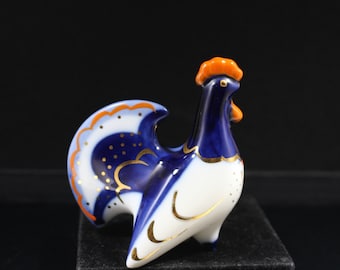May include: A blue and white porcelain rooster figurine with gold accents. The rooster has an orange comb and wattle.