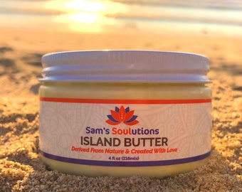 May include: A white jar with a red and orange label that says "Sam's Soulutions Island Butter Derived From Nature & Created With Love 4 fl oz (118mls)". The jar is sitting on a sandy beach.