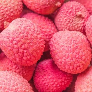 Op de afbeelding: Close-up van een groep roze lychees. De lychees hebben een ruwe, getextureerde schil en zijn in een cluster gerangschikt.