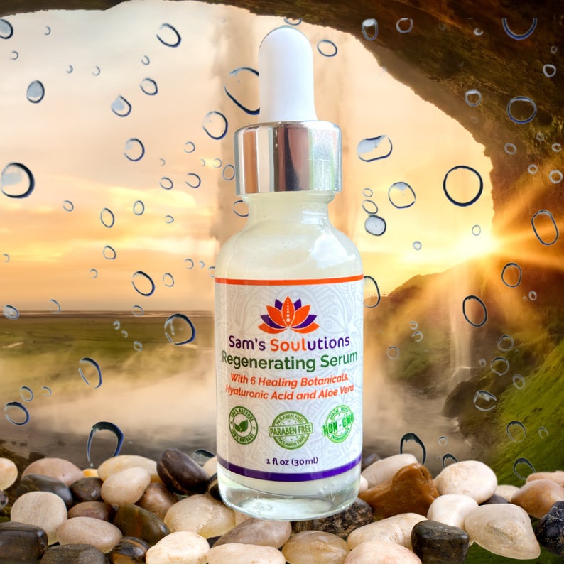 Op de afbeelding: Een doorzichtige glazen fles met Sam's Soulutions Regenerating Serum met een witte druppelaar. De fles is gelabeld met een wit en paars lotusbloemontwerp en de tekst "Sam's Soulutions Regenerating Serum" in zwart. De fles staat op een bed van gladde, grijze stenen. De fles is gelabeld met de tekst "With 6 Healing Botanicals, Hyaluronic Acid and Aloe Vera". De fles is ook gelabeld met de tekst "Paraben Free" en "Non-GMO". De fles is gelabeld met de tekst "1 fl oz (30ml)".