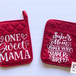 May include: Two red quilted pot holders with white text. One pot holder says "One Sweet Mama" with hearts. The other pot holder says "Super Mom Super Wife Super Tired" with stars.