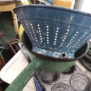 May include: A collection of vintage kitchenware, including a blue and white speckled enamel colander, a green speckled saucepan, and a muffin tin. The colander has numerous small holes for draining. Other items include bowls and plates.
