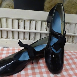May include: A pair of black patent leather dance shoes with a blue lining and black ribbon ties. The shoes have a metal tap on the toe.