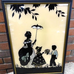 May include: A framed silhouette artwork depicting three figures: a woman holding an umbrella, a girl with a flower bouquet, and a boy. The figures are black against a cream background with a tree branch at the top.