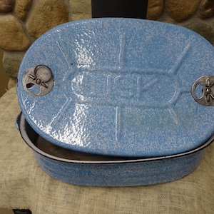 Peut inclure: Un plat à four en émail bleu avec un couvercle. Le couvercle a deux poignées métalliques avec un motif décoratif. Le plat est moucheté de points blancs.