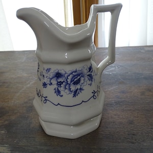 Könnte beinhalten: Eine weiße Keramikkanne mit blauem Blumendesign. Die Kanne hat einen Henkel und einen breiten Ausguss.