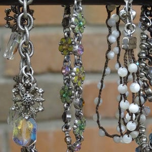 May include: A collection of silver-toned charm bracelets and necklaces with various decorative elements. The charms include beads, crystals, and floral designs. Some necklaces feature white beads and others have colorful accents.