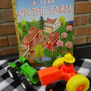 May include: A vintage children's book titled "A Year On The Farm" with a green and orange toy tractor and a toy farmer in a yellow hat.