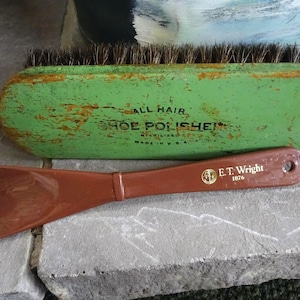 May include: An antique shoe shine kit with a green brush and a brown shoe horn. The brush is labeled "ALL HAIR SHOE POLISHER" and the shoe horn has the text "E.T. Wright 1876". The kit is likely vintage.