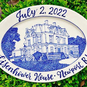 May include: An oval ceramic platter featuring a detailed blue ink illustration of the Eisenhower House in Newport, RI. The text "July 2, 2022" is printed at the top, and "Eisenhower House - Newport RI" is printed at the bottom in blue script.