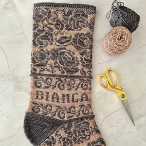 Pode incluir: Uma meia de tricô marrom e cinza com um padrão floral e a palavra "MANCA" bordada na bainha.