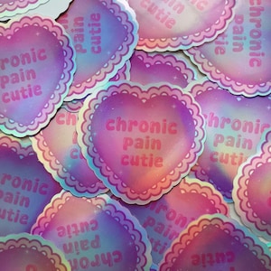 May include: A pile of heart-shaped stickers with a shimmering, holographic effect. Each sticker has a decorative, scalloped edge and the words "chronic pain cutie" in a pink, bubble font. The stickers have a gradient of pink, purple, and blue hues.