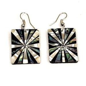 May include: A pair of square earrings with a sunburst design. The earrings feature a silver hook and a square pendant with a black, white, and iridescent pattern. The design radiates from the center of the square.