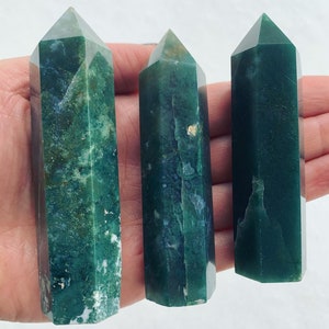 Puede incluir: Tres puntas de cristal de ágata verde, también conocidas como ágata verde musgo, se muestran en una mano. Las puntas están pulidas y tienen un acabado liso y brillante.
