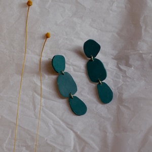 May include: A pair of teal blue statement earrings with three teardrop-shaped pieces connected by gold rings.