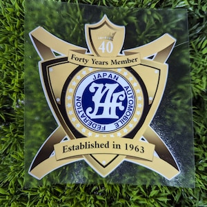 May include: A gold and blue sticker with the text "Forty Years Member" and a logo that says "Japan Automobile Federation" with the number "47" in the center. The sticker also says "Established in 1963".