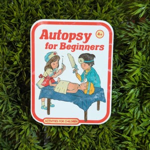 May include: A white sticker with a red border and the text "Autopsy for Beginners 4+" in red and black. The sticker features a cartoon illustration of two children performing an autopsy on a small child lying on a table. The text "Activities for Children" is at the bottom of the sticker.