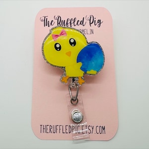 May include: A yellow chick with a pink bow holding a blue egg, glitter accents, on a pink card with the text "The Ruffled Pig" and "theruffledpig.etsy.com".