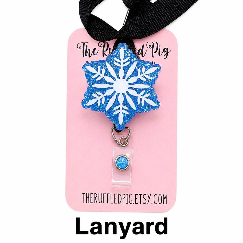 May include: A blue glittery snowflake badge reel attached to a black lanyard. The snowflake features a white center design. The badge is mounted on a light pink display card with the text The Ruffled Pig and theruffledpig.etsy.com printed on it.