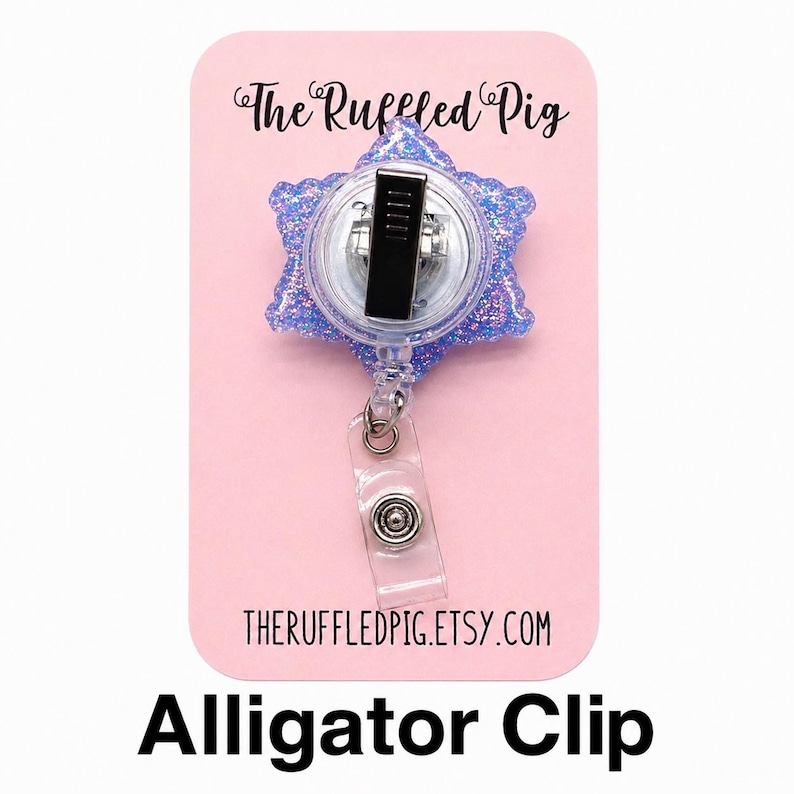 May include: A blue glittery snowflake-shaped badge reel featuring a metal alligator clip on the back and a clear plastic strap with a snap button. The item is mounted on a pink display card labeled The Ruffled Pig and theruffledpig.etsy.com.