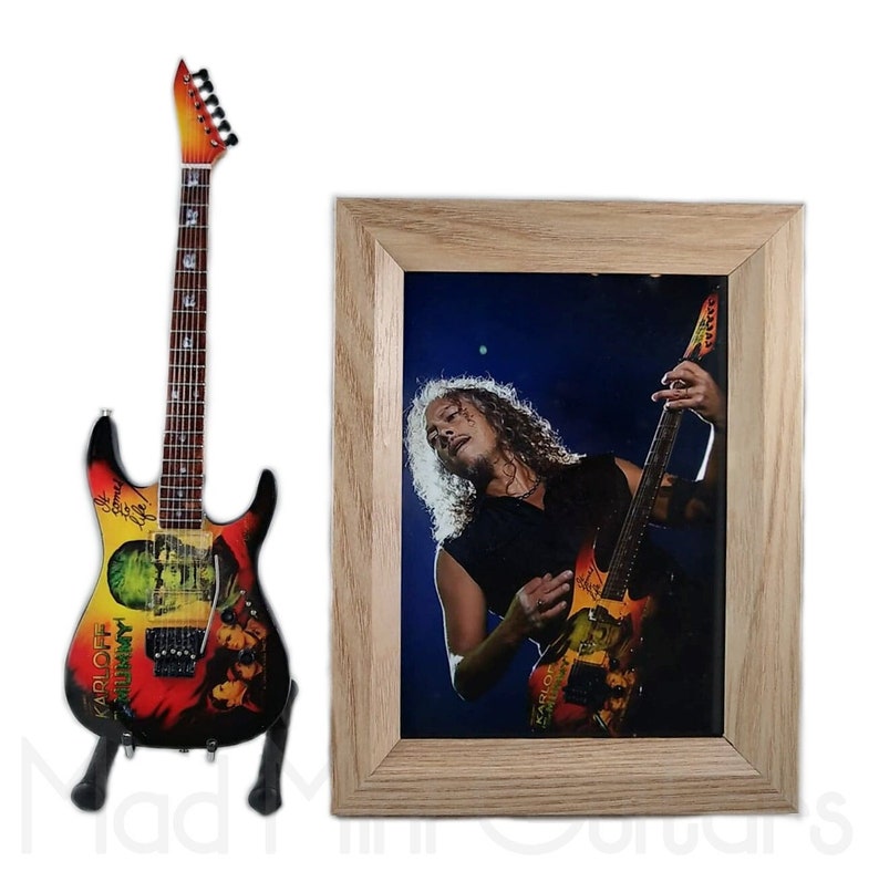 Pu&ograve; includere: Una replica in miniatura di una chitarra elettrica nera e arancione con una stampa grafica verde e rossa. La chitarra &egrave; su un supporto e c'&egrave; una foto incorniciata di un musicista che suona una chitarra simile.
