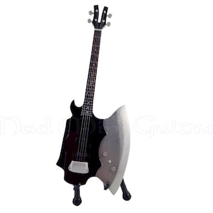 Puede incluir: Una guitarra eléctrica negra con un cuerpo en forma de hacha plateado. La guitarra está en un soporte negro.