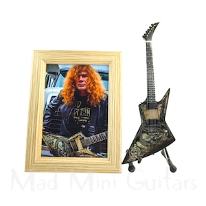 Peut inclure: Une photographie encadrée d'un musicien aux longs cheveux roux, portant une veste en cuir noire, tenant une guitare. À côté, une guitare électrique miniature noire et argentée sur un support. Le texte "Mad Mini Guitars" est visible.