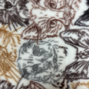May include: A white fabric with a repeating pattern of brown and gray animal faces. The fabric has a fuzzy texture.