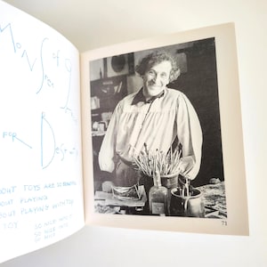 May include: A book page featuring a black and white photograph of a person with curly hair wearing a collared shirt with full sleeves. The page includes blue handwritten text that reads: ABOUT TOYS ARE SO BEAUTIFUL, ABOUT PLAYING, ABOUT PLAYING WITH TOY, A TOY, SO NICE INTO IT, SO NICE INTO, SO NICE.