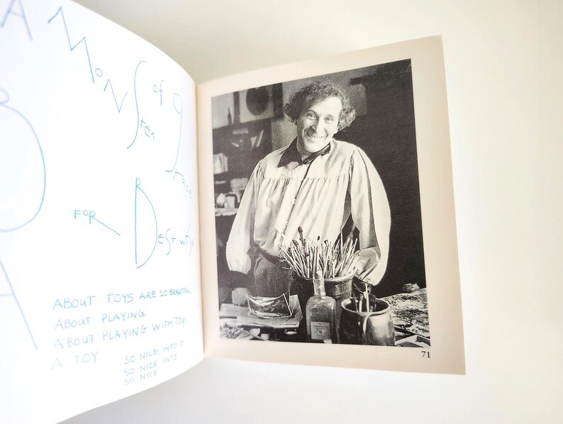 May include: A book page featuring a black and white photograph of a person with curly hair wearing a collared shirt with full sleeves. The page includes blue handwritten text that reads: ABOUT TOYS ARE SO BEAUTIFUL, ABOUT PLAYING, ABOUT PLAYING WITH TOY, A TOY, SO NICE INTO IT, SO NICE INTO, SO NICE.