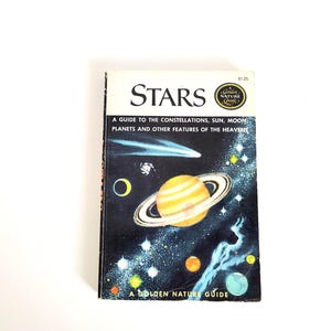 May include: A vintage paperback book titled Stars: A Guide to the Constellations, Sun, Moon, Planets and Other Features of the Heavens. The cover features a dark space background with a large ringed planet, a comet, and various stars.