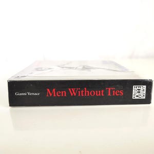 May include: A hardcover book titled Men Without Ties by Gianni Versace, featuring a black spine with red text and the Abbeville Press logo. The book is positioned horizontally, showing the side edge with clear white lettering and branding.