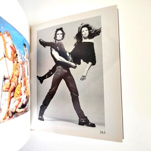 May include: A book page featuring two distinct images. On the left, a colorful illustration of figures with white horses. On the right, a black and white photograph of two individuals, one lifting the other, with the page number 263 printed below.