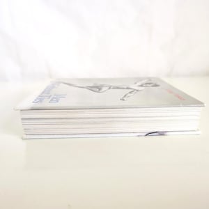May include: A rectangular book with a light gray cover featuring a black and white illustration of a figure in motion. The title Men Without Ties is printed in blue text on the left side, and the author name is in red text on the right side.