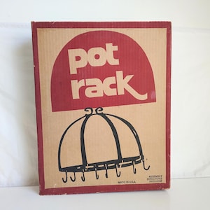 May include: A rectangular cardboard box for a pot rack. The box has a red arched design with the words "pot rack" in white. Below the text is a black illustration of a pot rack with hooks. The box is made in the USA.