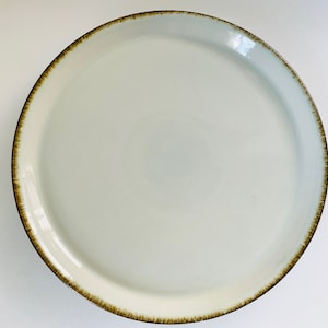 Puede incluir: Un plato de cerámica blanco con un borde marrón. El plato es redondo y tiene una superficie lisa.