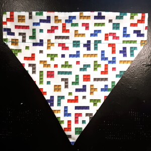 May include: A white triangular dog bandana with a colourful pixelated pattern. The bandana features a variety of colours including red, blue, green, yellow, and brown.