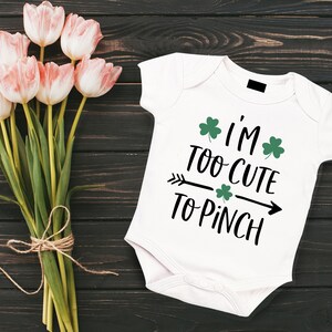 Peut inclure: Combinaison blanche pour b&eacute;b&eacute; avec un motif noir et vert qui dit "I'm Too Cute To Pinch" avec des tr&egrave;fles.