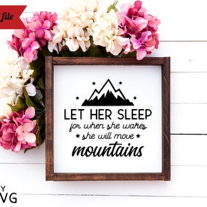 May include: A white sign with a brown wooden frame, featuring a black mountain silhouette with stars and the text "LET HER SLEEP for when she wakes * she will move * mountains".