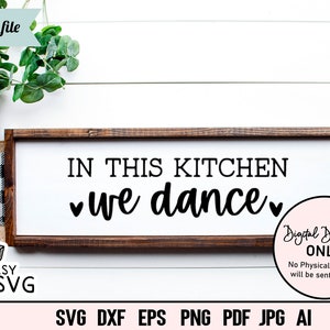 Puede incluir: Un letrero de madera marrón con el texto "In this kitchen we dance" en letras negras con un corazón a cada lado de la palabra "we". El letrero está sobre un fondo blanco con un patrón de cuadros blanco y negro a los lados izquierdo y derecho del letrero.