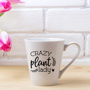 Op de afbeelding: Witte keramische mok met een zwart ontwerp met de tekst "Crazy plant lady" met een klein hartje en bladeren.