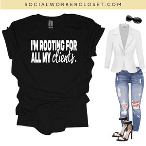 May include: Black t-shirt with the text "I'm rooting for all my clients."  A white blazer, distressed blue jeans, and black heeled sandals are shown in the background.