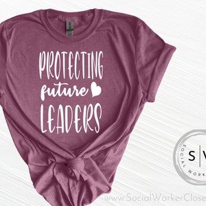 May include: A mauve t-shirt with the text "Protecting future leaders" in white with a white heart symbol. The shirt is tied in a knot at the bottom.